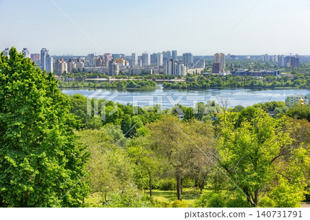 View of a city skyline along a river with green trees and clear sky during daytime on a sunny day View of a city skyline along a river with green trees and clear sky during daytime on a sunny day 140731791