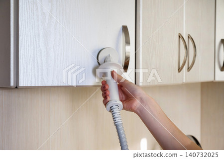 Using a kitchen appliance for cleaning on a cabinet surface in a modern home setup Using a kitchen appliance for cleaning on a cabinet surface in a modern home setup 140732025