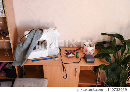 Sewing tools and materials on a desk near a sewing machine in a workspace Sewing tools and materials on a desk near a sewing machine in a workspace 140732059