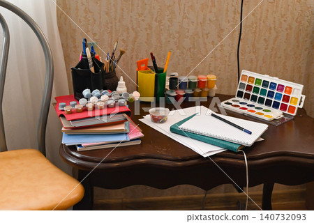 Art supplies are arranged on a wooden desk with paper, paints, and brushes in a creative workspace Art supplies are arranged on a wooden desk with paper, paints, and brushes in a creative workspace 140732093