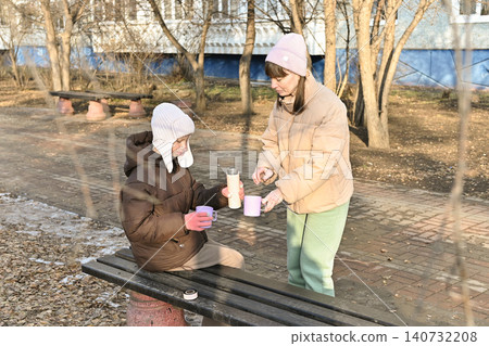 Two people share warm drinks in a park on a cool day with trees in the background Two people share warm drinks in a park on a cool day with trees in the background 140732208