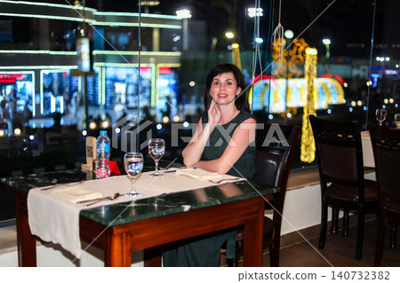 Elegant Woman Enjoying Dinner in a Restaurant with Stunning Night City View Through the Window, Capturing the Essence of Urban Sophistication 140732382