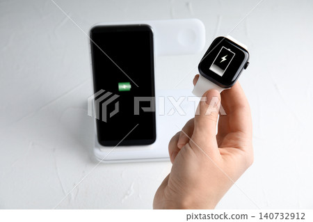 Woman taking smartwatch from wireless charger at white stone table, closeup 140732912