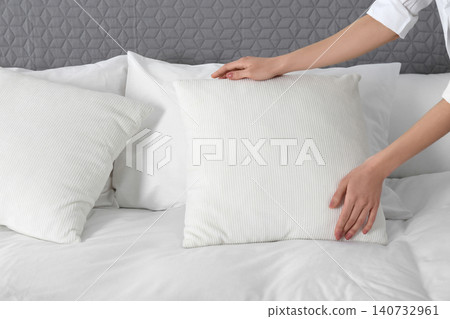 Woman fluffing soft pillow in bedroom, closeup Woman fluffing soft pillow in bedroom, closeup 140732961