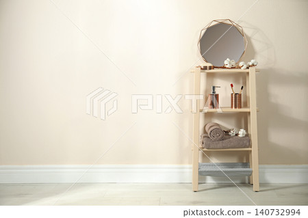 Wooden shelving unit with toiletries near beige wall indoors, space for text. Bathroom interior element Wooden shelving unit with toiletries near beige wall indoors, space for text. Bathroom interior element 140732994