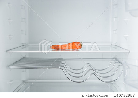 Old carrot on empty shelf in refrigerator 140732998
