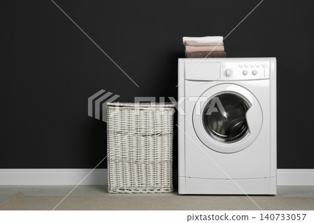 Modern washing machine and laundry basket near black wall Modern washing machine and laundry basket near black wall 140733057