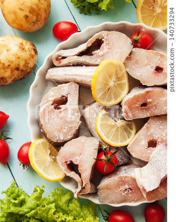 Fresh pollock seafood steaks with lettuce and cherry tomatoes seasoned with salt and lemon in pan. Fresh pollock seafood steaks with lettuce and cherry tomatoes seasoned with salt and lemon in pan. 140733294