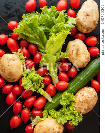 Red ripe fresh cherry tomatoes, lettuce, potatoes and cucumber on black background with water drops Red ripe fresh cherry tomatoes, lettuce, potatoes and cucumber on black background with water drops 140733302