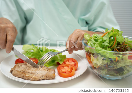 Asian elderly woman patient eating pork chop stake and vegetable salad for healthy food in hospital. Asian elderly woman patient eating pork chop stake and vegetable salad for healthy food in hospital. 140733335