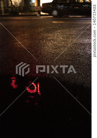 在雨中的新宿街道上,丸井百貨的紅色霓虹燈招牌扭曲地倒映在水坑如鏡的表面上。 在雨中的新宿街道上,丸井百貨的紅色霓虹燈招牌扭曲地倒映在水坑如鏡的表面上。 140733488