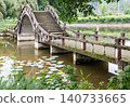 A timeless stone bridge arches over a tranquil, lily-dappled pond at Dazu Lotus Manor. The central span rises into a dramatic curve like a traditional Chinese moon bridge. Weathered steps climb 140733665