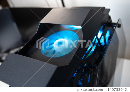 Computer cooling fan with bright blue led light installed in an iron gaming pc case. Modern hardware for air circulation and temperature control in high performance desktop pc machine. Computer cooling fan with bright blue led light installed in an iron gaming pc case. Modern hardware for air circulation and temperature control in high performance desktop pc machine. 140733942
