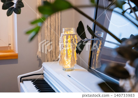 Macrame lamp with glowing fairy lights inside glass vase on piano. Cozy home interior decoration for evening atmosphere. Handmade bohemia style craft project for room lighting. 140733983