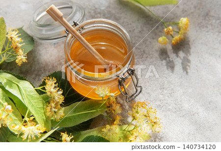 Linden honey jar with wooden dipper and fresh flowers Linden honey jar with wooden dipper and fresh flowers 140734120