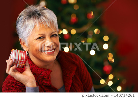 Portrait, Christmas and present for mature woman, smile and box for celebration. Tree, decoration and gift for Christian holiday, happy or package for special family event for senior female at home 140734261
