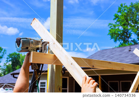 Worker assembling wooden frame with pneumatic nailer during outdoor shed construction project, 140734336