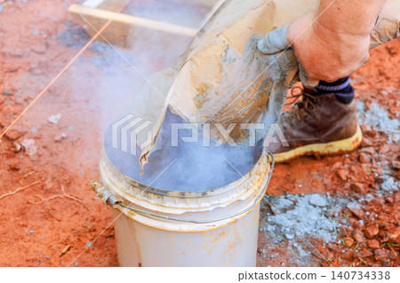 Worker holds bag, pours dry cement into bucket on construction site Worker holds bag, pours dry cement into bucket on construction site 140734338