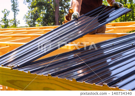 Worker lays metal roofing panels on wooden beams frame as project progresses in summer. Worker lays metal roofing panels on wooden beams frame as project progresses in summer. 140734340