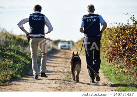 Policeman, dog and walk in field for crime scene or robbery with car for search, safety and law enforcement. Detective, investigation and uniform in outdoor working at countryside with gravel road Policeman, dog and walk in field for crime scene or robbery with car for search, safety and law enforcement. Detective, investigation and uniform in outdoor working at countryside with gravel road 140735427