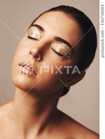 Woman, face and gold glitter eyeshadow for beauty, cosmetology and glamour with cosmetics on beige background. Makeup, elegance and fashion model in studio, art or creativity with shimmer and glow Woman, face and gold glitter eyeshadow for beauty, cosmetology and glamour with cosmetics on beige background. Makeup, elegance and fashion model in studio, art or creativity with shimmer and glow 140736004