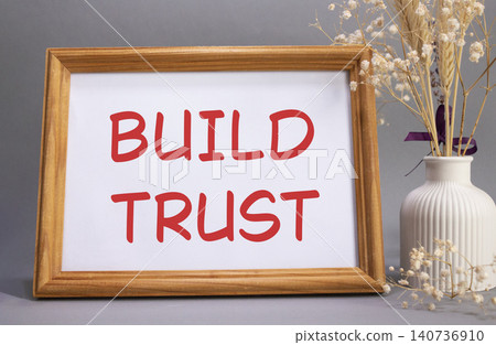 Build trust symbol. Concept words Build trust on beautiful wooden picture frame. Beautiful grey background with flower vase. Business and Build trust concept. Copy space. Build trust symbol. Concept words Build trust on beautiful wooden picture frame. Beautiful grey background with flower vase. Business and Build trust concept. Copy space. 140736910