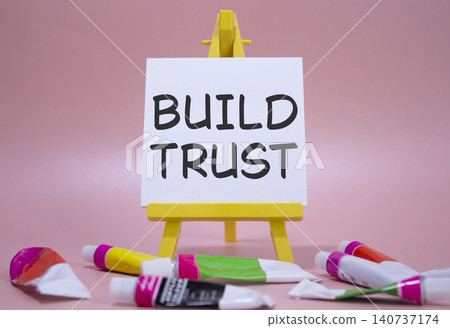 Build trust symbol. Wooden blocks with words Build trust. Beautiful pink background with paints and easel. Business and Build trust concept. Copy space. Build trust symbol. Wooden blocks with words Build trust. Beautiful pink background with paints and easel. Business and Build trust concept. Copy space. 140737174