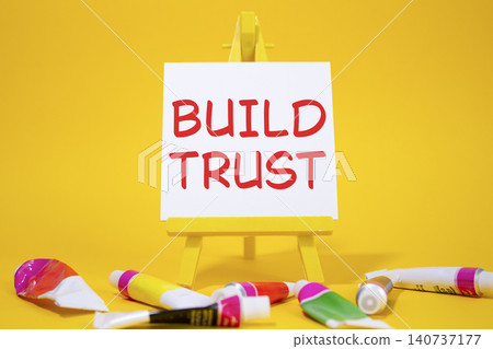 Build trust symbol. Wooden blocks with words Build trust. Beautiful yellow background with paints and easel. Business and Build trust concept. Copy space. Build trust symbol. Wooden blocks with words Build trust. Beautiful yellow background with paints and easel. Business and Build trust concept. Copy space. 140737177