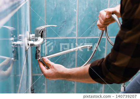 a man is doing repairs. The skilled handyman and homeowner perform a faucet replacement, effectively replacing an old faucet for home renovation. a man is doing repairs. The skilled handyman and homeowner perform a faucet replacement, effectively replacing an old faucet for home renovation. 140739207