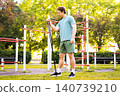 A man is doing a fitness workout with a resistance band outdoors in a sunny park. This strength training exercise builds muscle and promotes an active lifestyle. 140739210
