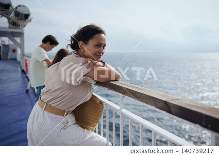 A woman leans on the ferry rail, gazing across the calm sea and horizon while enjoying a peaceful cruise vacation and contemplative moment on the ship's deck. A woman leans on the ferry rail, gazing across the calm sea and horizon while enjoying a peaceful cruise vacation and contemplative moment on the ship's deck. 140739217