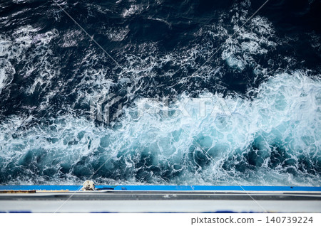 Turbulent deep-blue ocean seen from a ship railing, showing foamy wake, swirling waves and contrast between dark sea and white surf, conveying motion, power and maritime travel. Turbulent deep-blue ocean seen from a ship railing, showing foamy wake, swirling waves and contrast between dark sea and white surf, conveying motion, power and maritime travel. 140739224