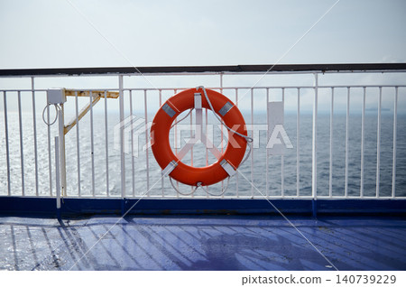 Bright orange life ring secured to a white ship railing with the open sea in the background, conveying safety, travel, marine and nautical calm on a clear sunny day. 140739229