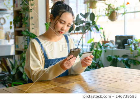 A woman pays with her smartphone and card at a cafe. A woman pays with her smartphone and card at a cafe. 140739583