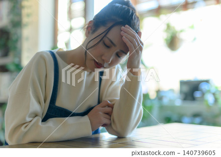 A young Japanese woman with her hand on her forehead, deep in thought. 140739605