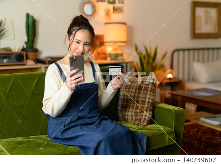A woman in the living room holding her smartphone and a card. A woman in the living room holding her smartphone and a card. 140739607