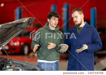 guy talks to a car service mechanic about car repairs guy talks to a car service mechanic about car repairs 140739706