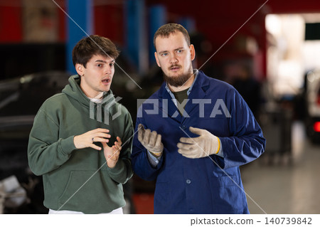 guy talks to a car service mechanic about car repairs guy talks to a car service mechanic about car repairs 140739842