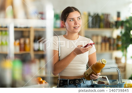 European young woman customer at shop scans QR code on peach juice bottle using phone camera European young woman customer at shop scans QR code on peach juice bottle using phone camera 140739845