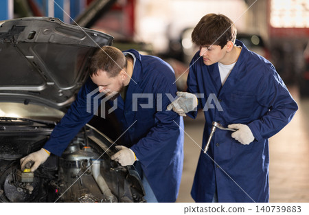 Two auto mechanics work together to diagnose an engine under the hood of a car in repair shop Two auto mechanics work together to diagnose an engine under the hood of a car in repair shop 140739883