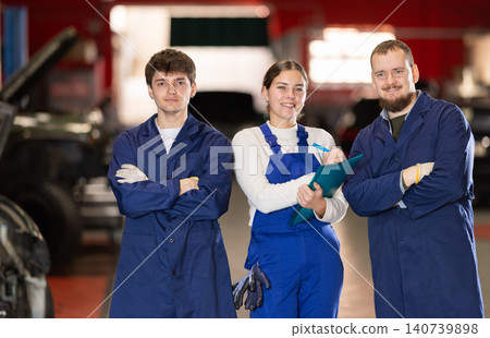 Team of auto mechanics, two men and one woman, wearing blue overalls and posing, ready to provide professional vehicle service Team of auto mechanics, two men and one woman, wearing blue overalls and posing, ready to provide professional vehicle service 140739898