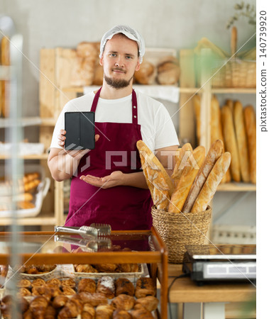 Young male bakery seller showing information on phone Young male bakery seller showing information on phone 140739920