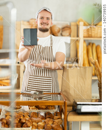 Young male bakery seller showing information on phone 140739935