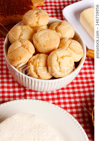 Homemade cheese bread served in a ceramic bowl, accompanied by fresh cheese and cornbread, set on a traditional Brazilian checkered tablecloth Homemade cheese bread served in a ceramic bowl, accompanied by fresh cheese and cornbread, set on a traditional Brazilian checkered tablecloth 140739956
