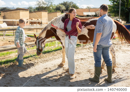 Family with child taking care of horse in pasture of horse farm Family with child taking care of horse in pasture of horse farm 140740000