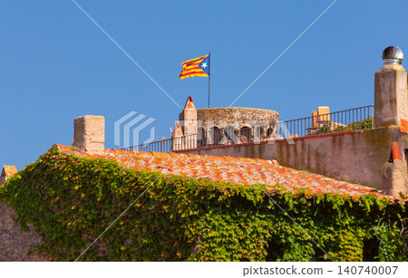Catalan flag flying above the historic stone walls and tiled rooftops of Tossa de Mar on the Costa Brava. 140740007