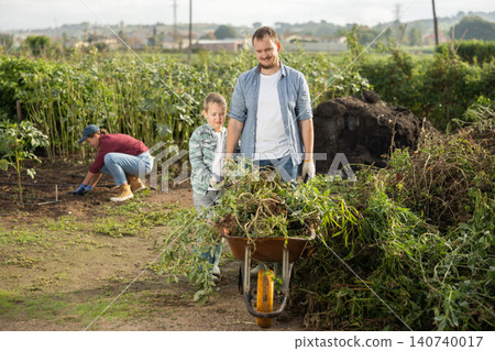 man and his son collect branches in a garden 140740017