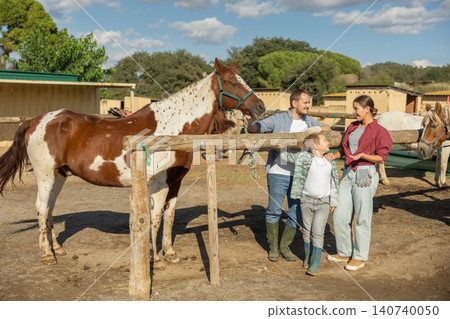 Father, mother and son riding horse together at small horse farm Father, mother and son riding horse together at small horse farm 140740050
