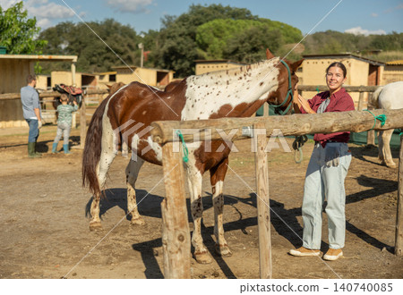Happy young girl preparing horse for riding and walking in pasture on farm 140740085