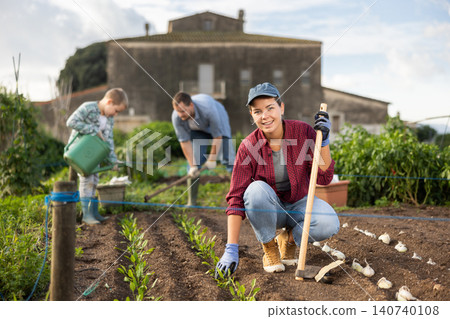 Woman with a garden tool near the beds in the garden Woman with a garden tool near the beds in the garden 140740108